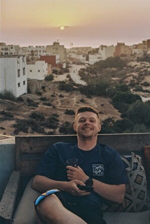 A person sitting on a balcony with a view of a cityscape during sunset.