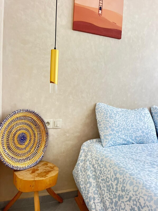 A bedroom with a bed, a wall-mounted light, a patterned rug, and a small wooden stool.