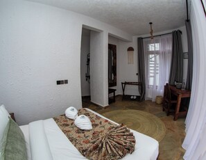 A hotel room with a bed, a small desk, a chair, a shower area, and a view of the outdoors. - Olarashii River Lodge (Arusha)