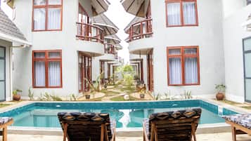 Uma área à beira da piscina com espreguiçadeiras, uma piscina e um edifício com várias varandas.