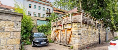 A black car parked in a narrow alleyway with stone walls and a wooden gate.