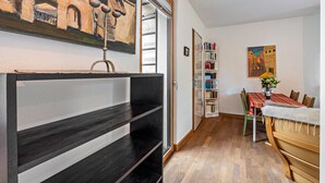 A room with a dark wooden bench, a bookshelf, a dining table with chairs, and a painting on the wall.