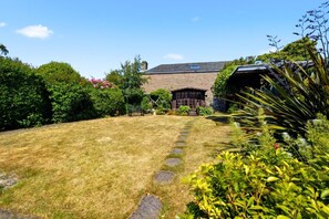 A garden with a stone pathway leading to a building with a sloped roof.