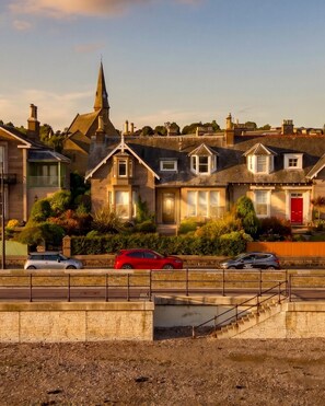 A residential area with houses, a church spire, and a road with parked cars.