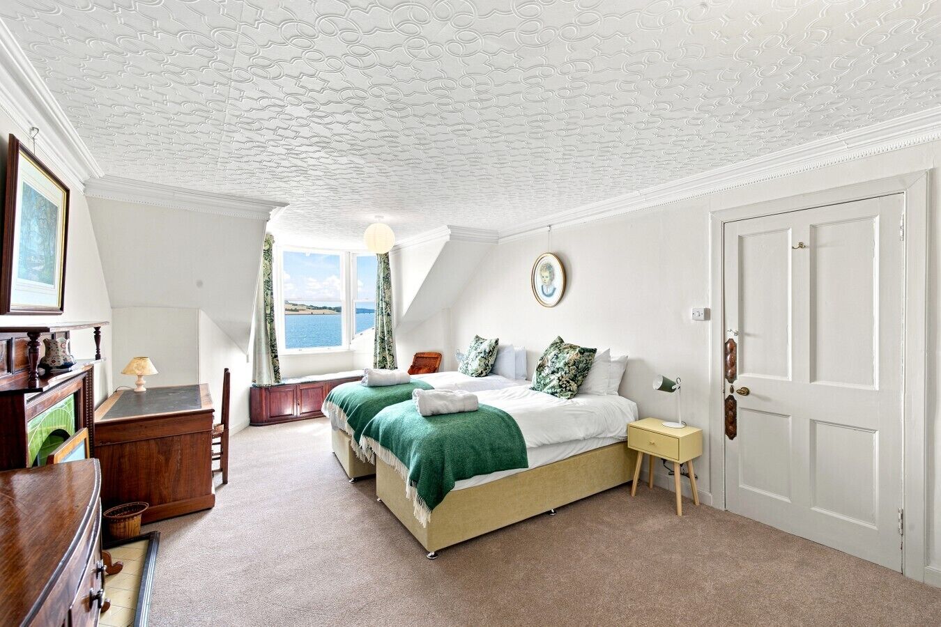 Une chambre à coucher avec un lit, un bureau, une chaise, une fenêtre donnant sur un paysage agréable et une porte.