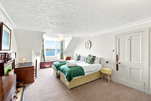 A bedroom with a bed, a desk, a chair, a window with a view, and a door.