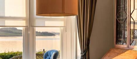 A room with a wooden table, a blue armchair, a lamp, and a view of the outdoors.