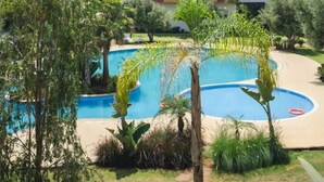 Un hotel de varios pisos con piscina rodeada de vegetación.