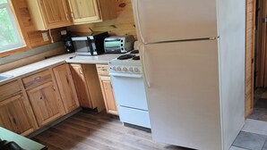 A wooden-paneled kitchen with a refrigerator, stove, microwave, and wooden cabinets. - Marvelous 2-bedroom cabin (Logan)