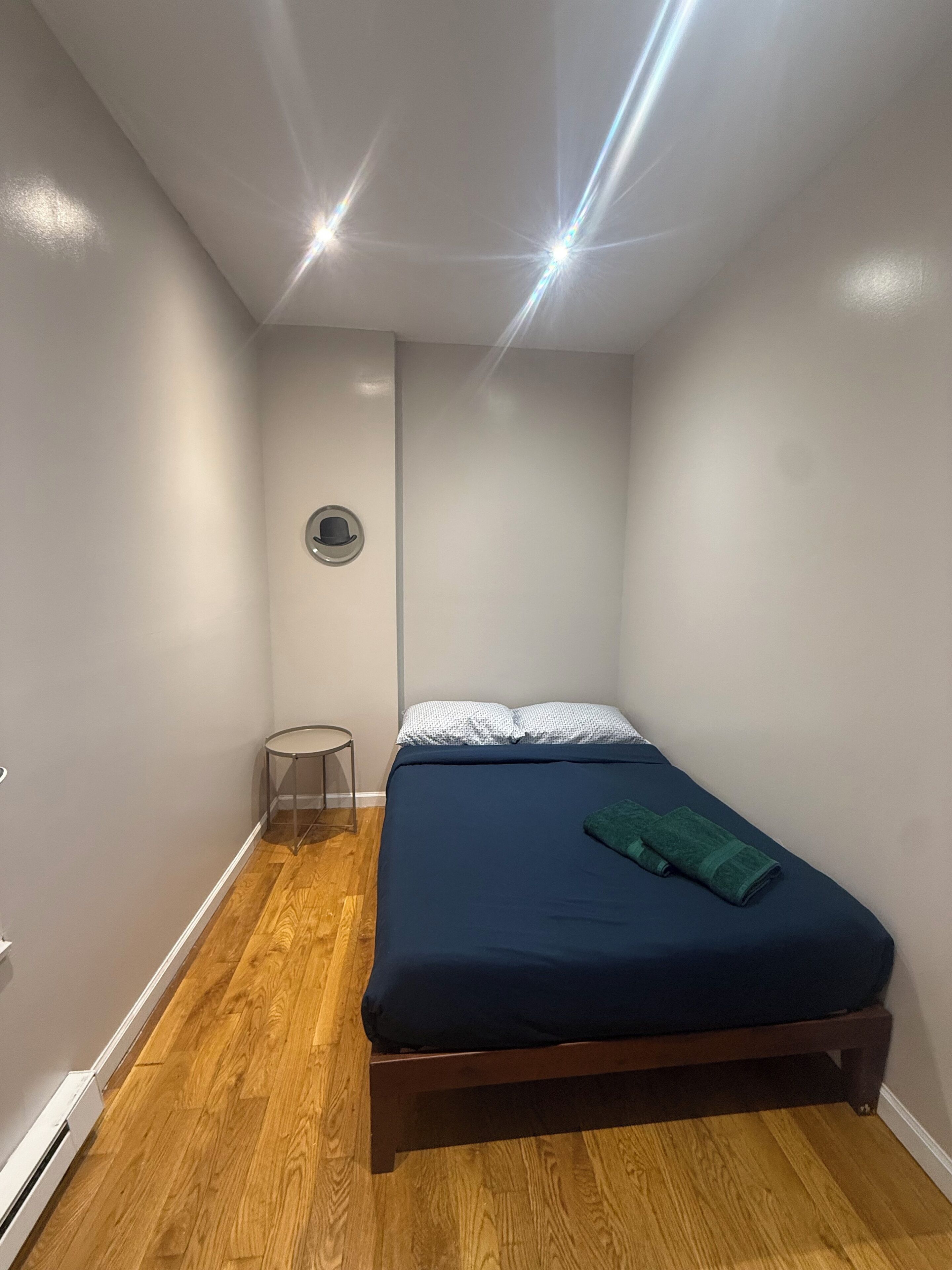 Une petite chambre à coucher, bien rangée, avec un lit, une petite table ronde et un porte-chapeaux fixé au mur.