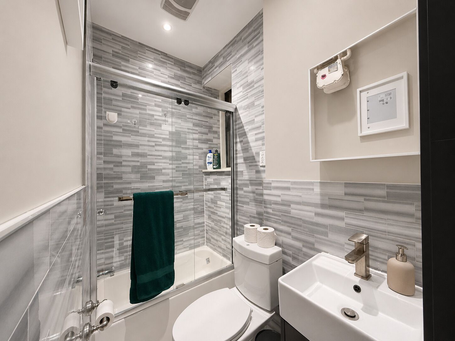 A modern bathroom with a glass-enclosed shower, a white toilet, a sink with a mirror, and a towel rack with a green towel.