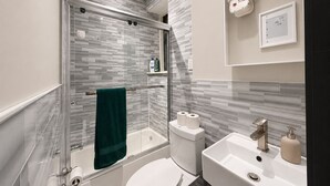 A modern bathroom with a glass-enclosed shower, a white toilet, a sink with a mirror, and a towel rack with a green towel. - Discover the Comfort of Columbia University Area-2 (New York)