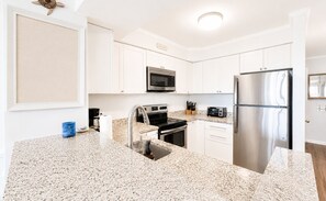 A modern kitchen with white cabinetry, stainless steel appliances, and a granite countertop. - Dunescape Villas 108 (Atlantic Beach)