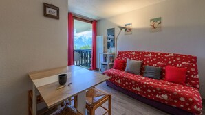 Ett mysigt rum med ett träbord, en röd soffa med ett blommönster och en utsikt över bergen genom ett fönster.