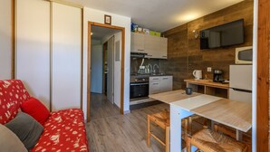 Ett kompakt bostadsutrymme med ett litet kök, en matplats och en soffa med mönstrade kuddar.