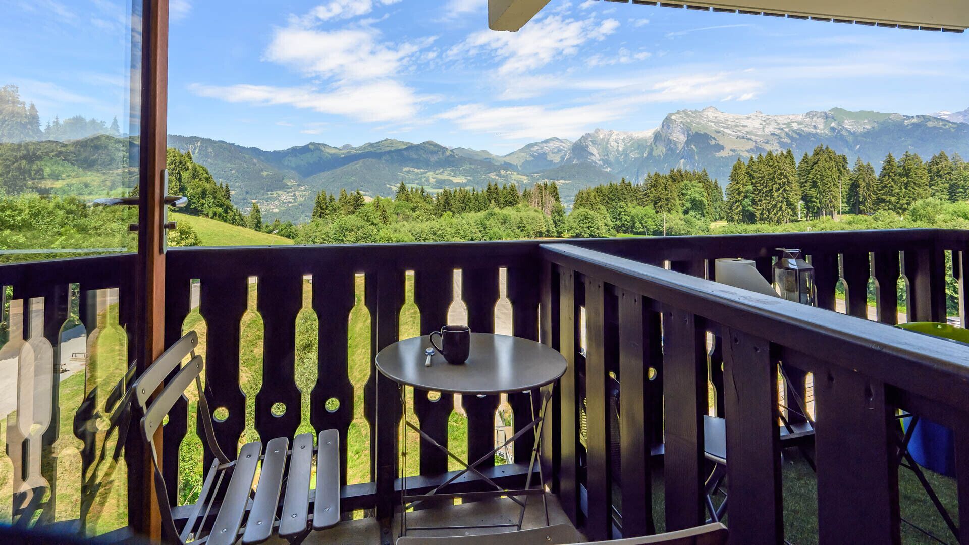 A balcony with a table and chairs, overlooking a mountainous landscape.