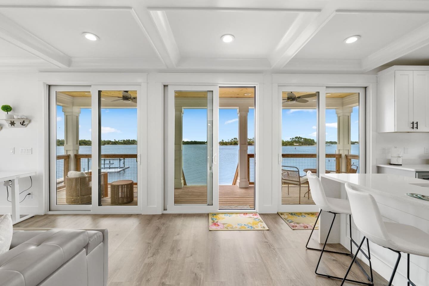 A modern interior with a kitchen, dining area, and large sliding glass doors leading to a deck with a view of a lake.