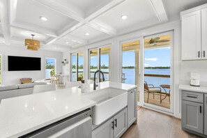 Une cuisine moderne dotée d’un grand îlot central, de meubles blancs et offrant une vue sur l’eau.