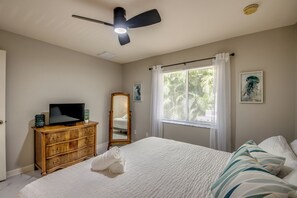 Ein Schlafzimmer mit einem Bett, einem Schminktisch, einem Deckenventilator, einem Fenster mit Vorhängen und einem Spiegel.