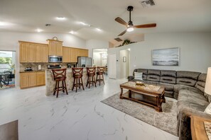 A spacious living area with a large sofa, a coffee table, and a kitchen with wooden cabinets and a bar stool area. - Tropical Paradise-Salt Water Pool-Billiards-Pool Volley/Basket Ball-Sleeps 8 (Cape Coral)
