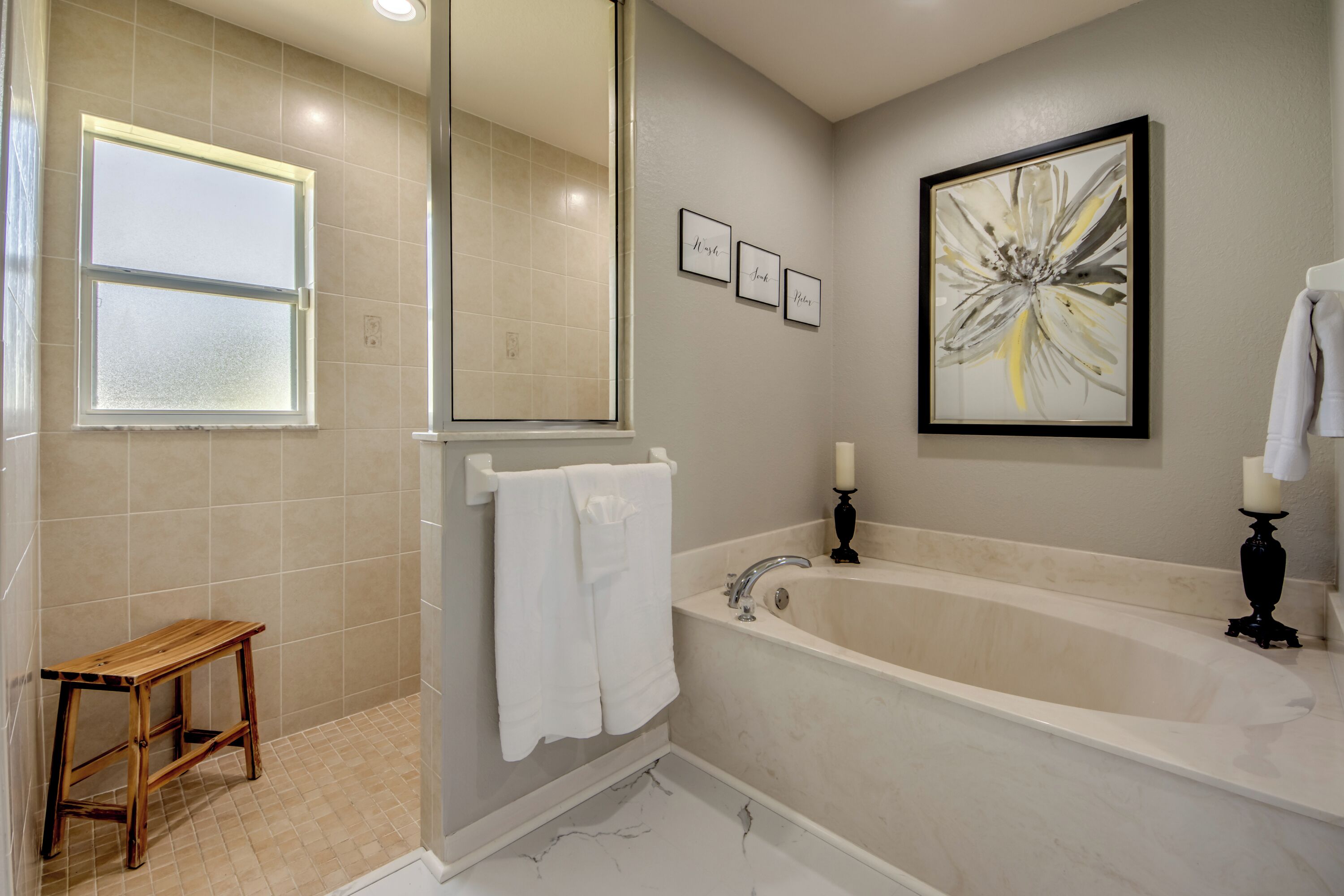 Une salle de bain avec une baignoire, un miroir, un porte-serviettes et un tableau abstrait encadré.