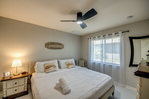 A bedroom with a bed, bedside tables, a lamp, a ceiling fan, and a window with curtains. - Tropical Paradise-Salt Water Pool-Billiards-Pool Volley/Basket Ball-Sleeps 8 (Cape Coral)