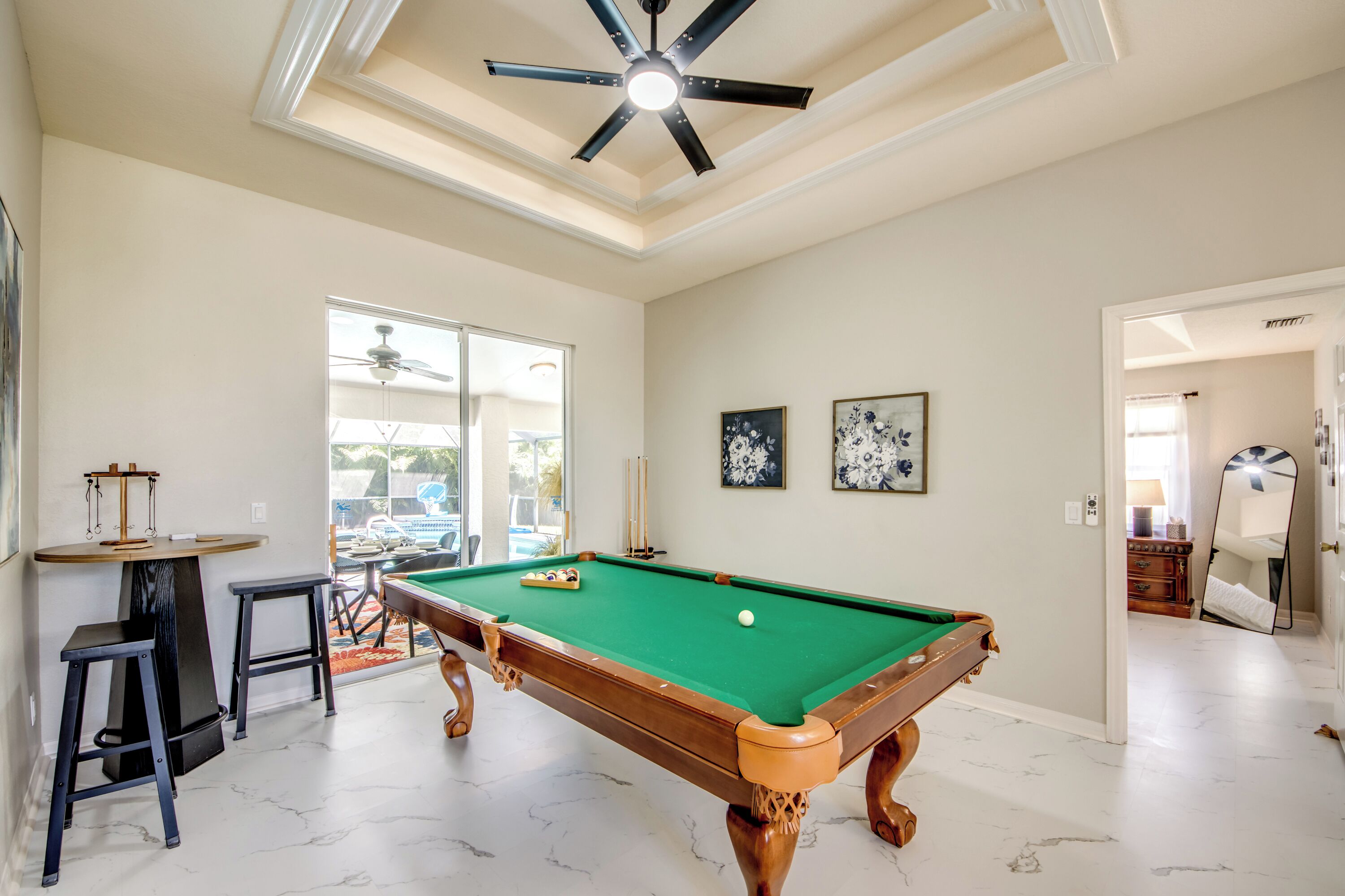 A pool table with a ceiling fan, a billiards rack, and a bar area with stools.