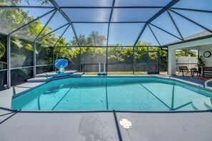 Ein klares, blaues Schwimmbecken mit Glasveranda, umgeben von einer Terrasse mit Gartenmöbeln.