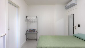 Ett rum med en våningssäng, en enkelsäng med ett grönt överkast, en vit dörr och en väggmonterad luftkonditioneringsanläggning.