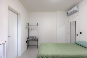 Ein Zimmer mit einem Etagenbett, einem Einzelbett mit grüner Bettdecke, einer weißen Tür und einer wandmontierten Klimaanlage.