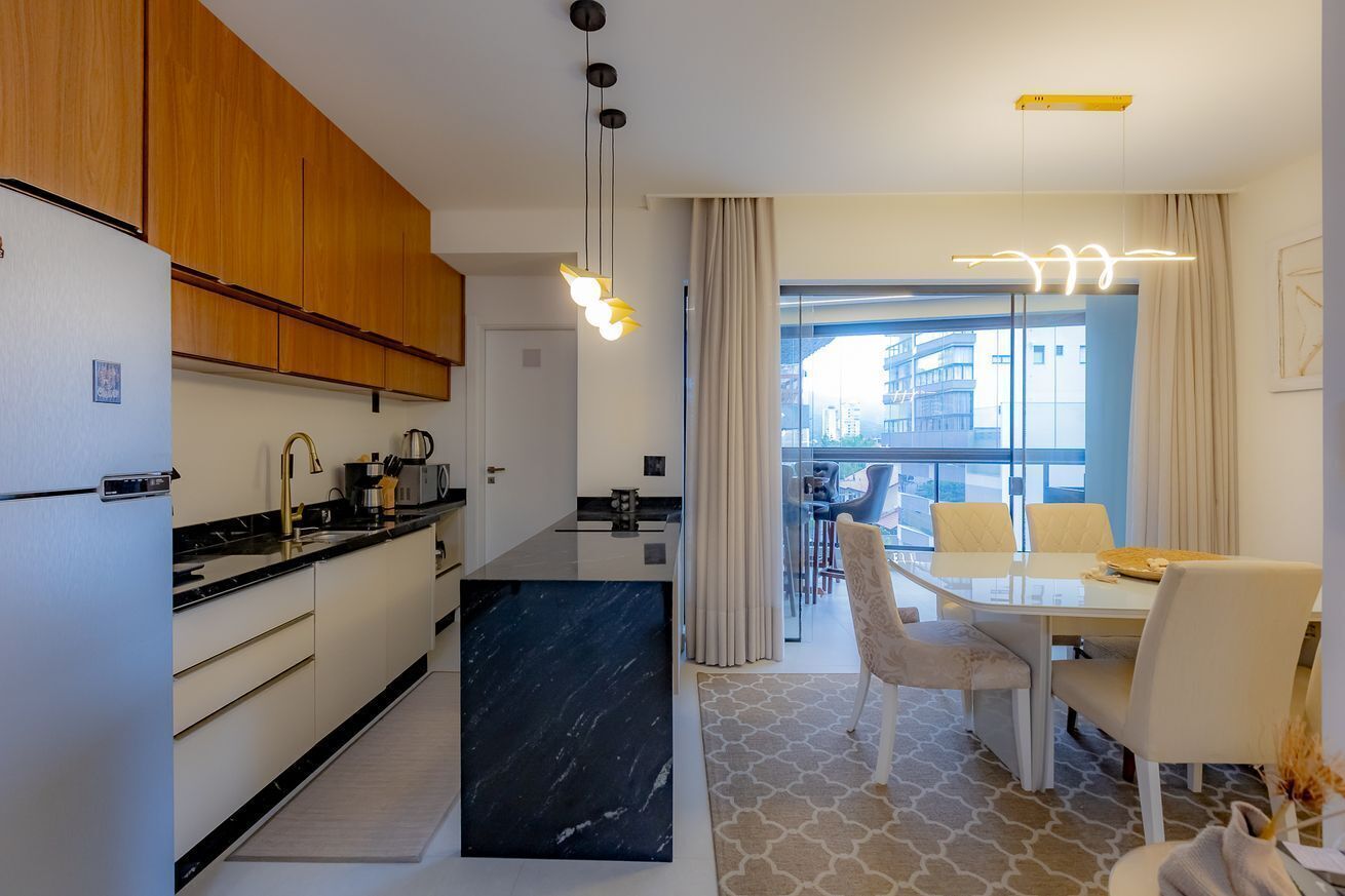 Een moderne keuken met houten kasten, een zwart marmeren eiland, en een eetgedeelte met een glazen tafel en stoelen.