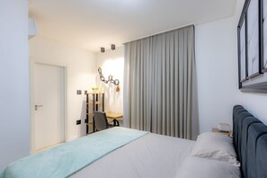 Une chambre d’hôtel avec un lit, un bureau, une chaise et une grande fenêtre avec des rideaux.