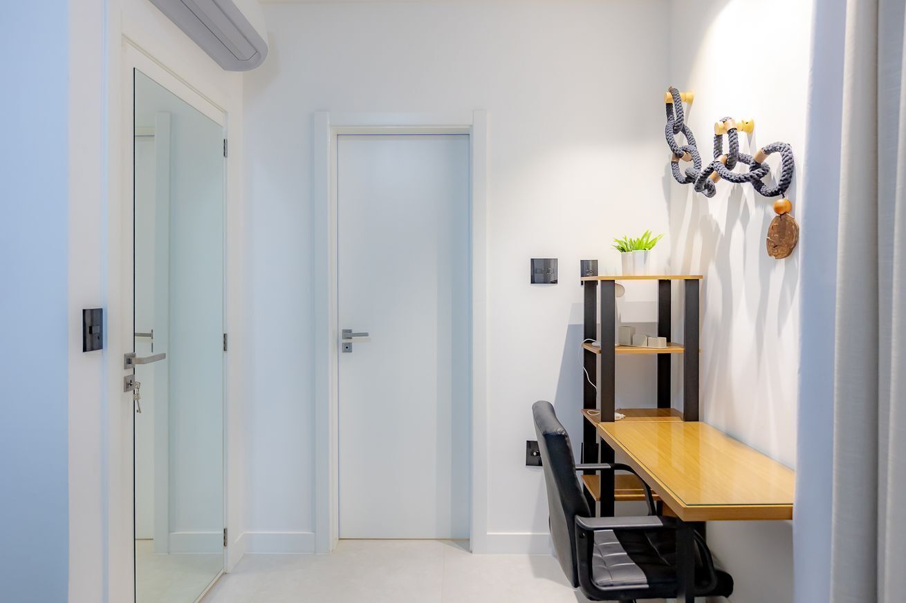 A modern room with a glass door, a wooden table, a black chair, and a wall-mounted shelf with decorative items.