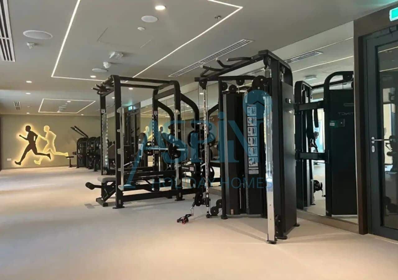 A gym with various exercise machines, a wall with a running figure, and a ceiling with recessed lighting.