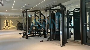 A gym with various exercise machines, a wall with a running figure, and a ceiling with recessed lighting. - Spacious 2 bedroom at Creek Edge - All Bills Included for long stay (Dubai)