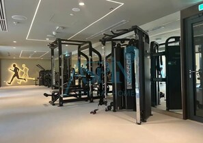 A gym with various exercise machines, a wall with a running figure, and a ceiling with recessed lighting. - Spacious 2 bedroom at Creek Edge - All Bills Included for long stay (Dubai)