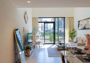 A modern living room with a large window, a dining area with a table set for two, and a seating area with a sofa. - Spacious 2 bedroom at Creek Edge - All Bills Included for long stay (Dubai)