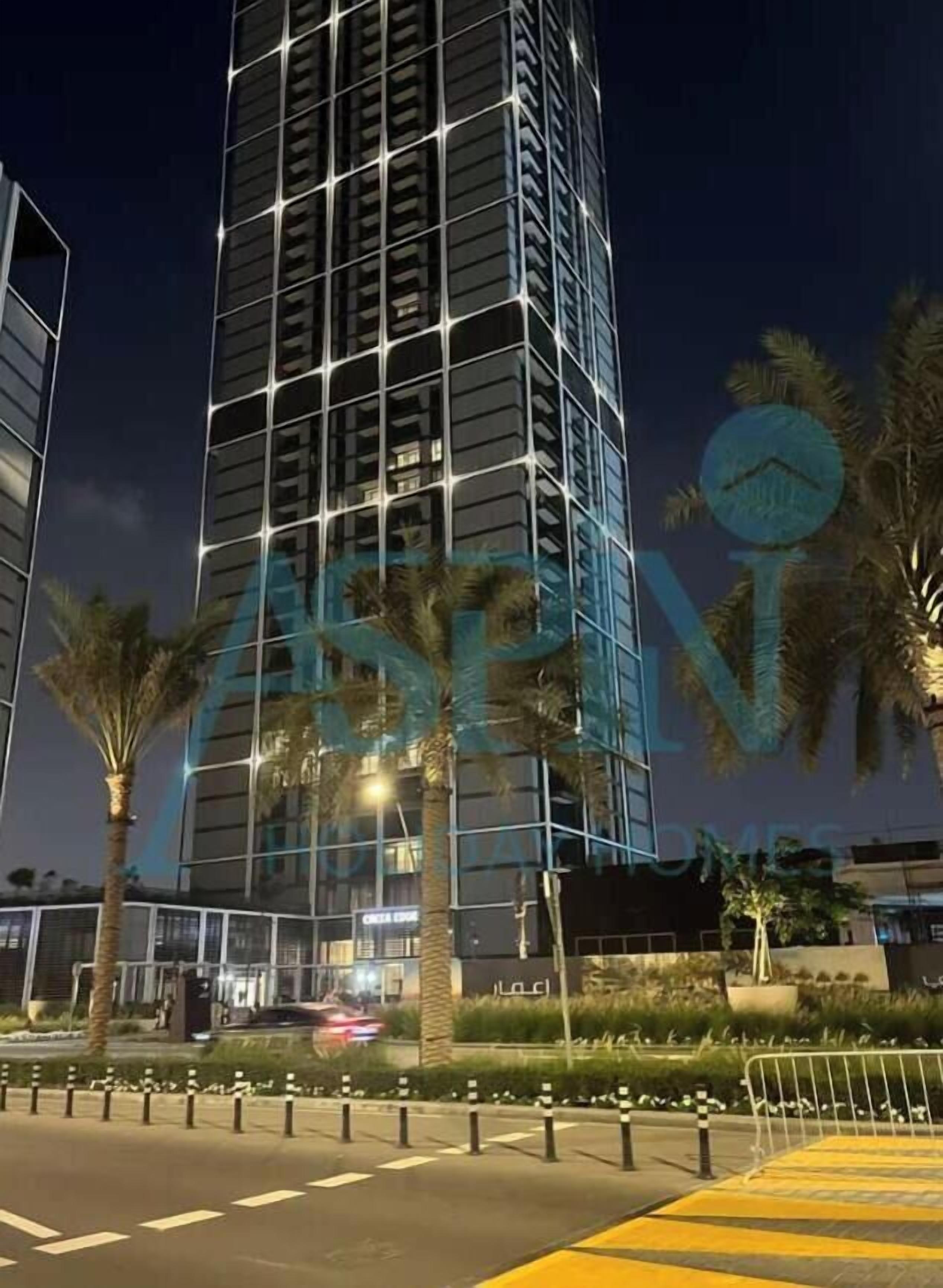 A modern high-rise building with a glass facade, surrounded by palm trees and a well-maintained landscaped area.