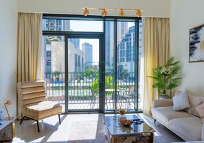 A modern living room with a sofa, a chair, a coffee table, and a balcony with a view of tall buildings. - Spacious 2 bedroom at Creek Edge - All Bills Included for long stay (Dubai)