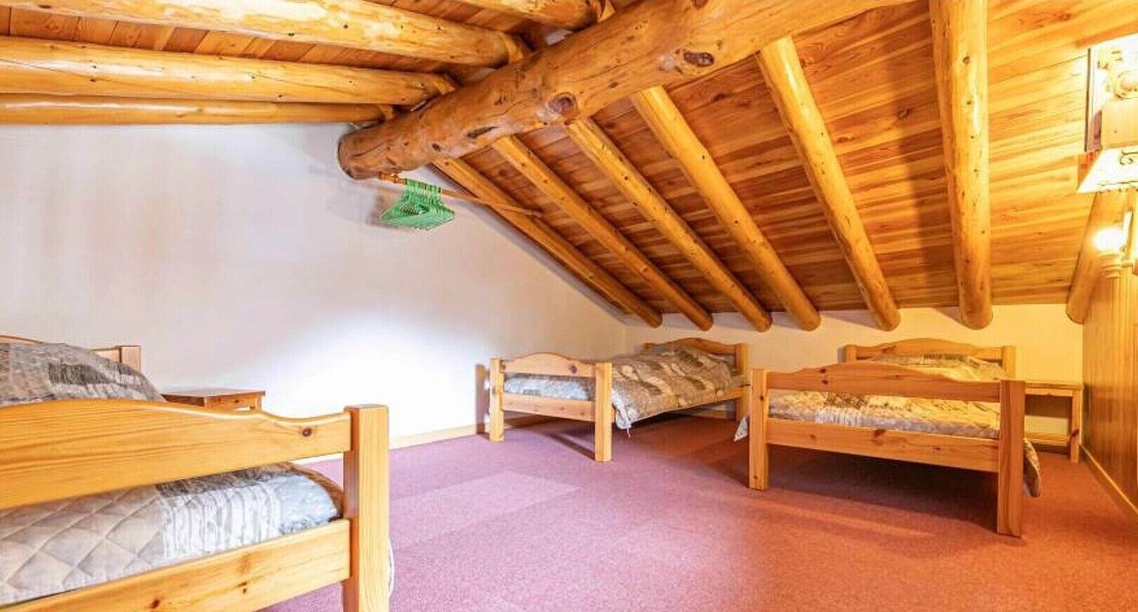 Een kamer met een schuine hemel, houten balken en drie stapelbedden.