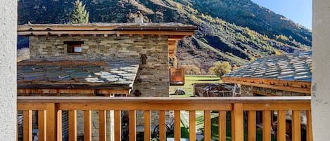 Un bâtiment en pierre doté d’un balcon en bois qui offre une vue sur un paysage montagneux.