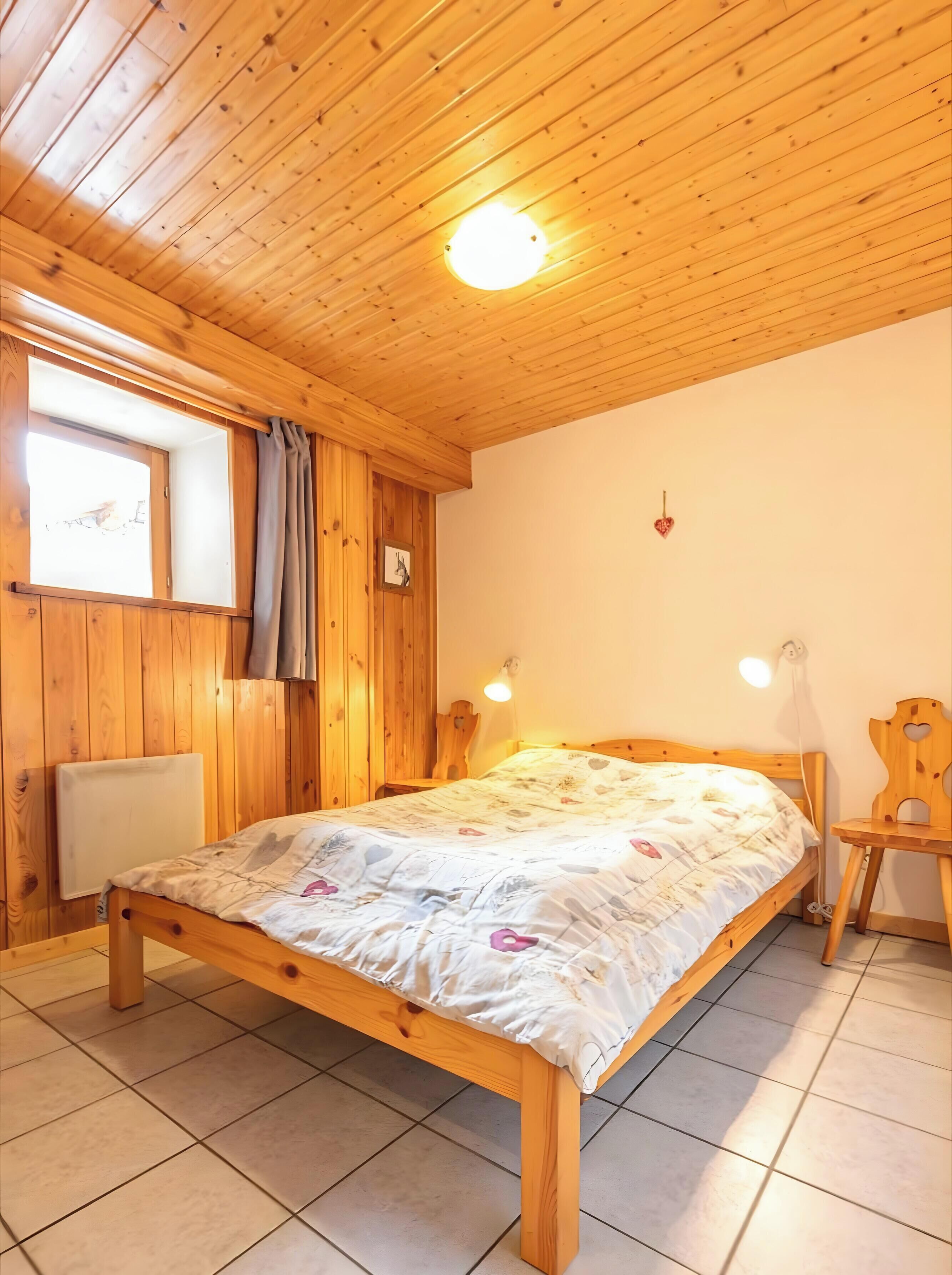 Une pièce aux murs lambrissés, avec un lit, une fenêtre avec des rideaux, une horloge murale et un petit bureau avec une chaise.