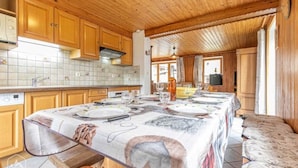 A wooden interior with a dining table set for four, kitchen cabinets, and a tiled backsplash.