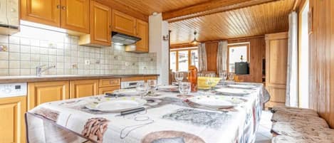 A wooden interior with a dining table set for four, kitchen cabinets, and a tiled backsplash.