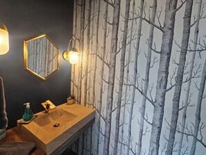 Un baño con tocador de madera, espejo montado en la pared y pared con diseño de árboles.