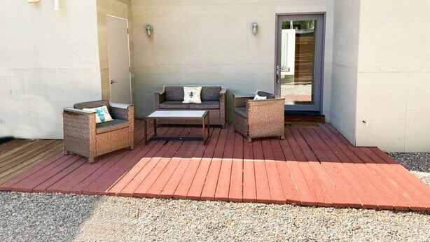 A covered outdoor seating area with wicker furniture, a wooden table, and a door leading to a building. - Private Luxury Modern Design with NM charm: Gourmet Kitchen & Spa Bath! (Taos)