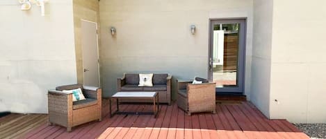 A covered outdoor seating area with wicker furniture, a wooden table, and a door leading to a building.
