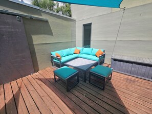 Eine Terrasse im Freien mit Holzdeck, einem türkisfarbenen Sofa mit orangefarbenen Kissen und passenden Hocker.