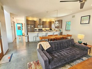 Eine moderne Küche mit Kochinsel, Essbereich mit einer Couch und Stühlen sowie ein Wohnzimmer mit einem großen grauen Sofa.