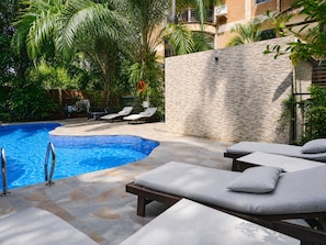 A swimming pool with lounge chairs and a stone wall. - 2-bedroom apartment with Garden view (Accra)